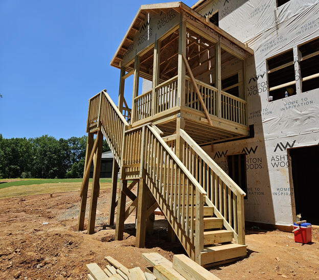 Elevated Wood Deck Elevated wood deck with structural support posts, cross bracing, and stair system installed beside a residential home. Call or text Raleigh Outdoor Spaces for a free consultation.