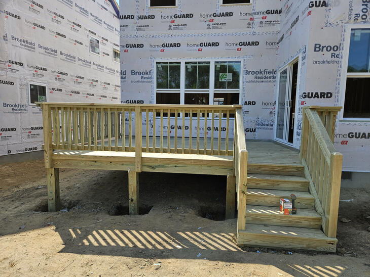 Newly constructed pressure-treated wood deck attached to a residential home with stairs and railings. Call or text Raleigh Outdoor Spaces for a free consultation.